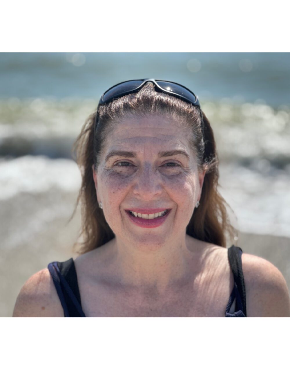 Smiling woman at the beach with sunglasses on her head.